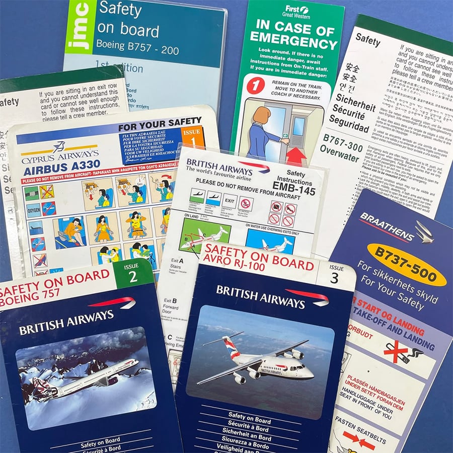 A collection of various airline safety cards from different airlines and aircraft models, spread out on a blue background. The cards have colorful illustrations and text in multiple languages.