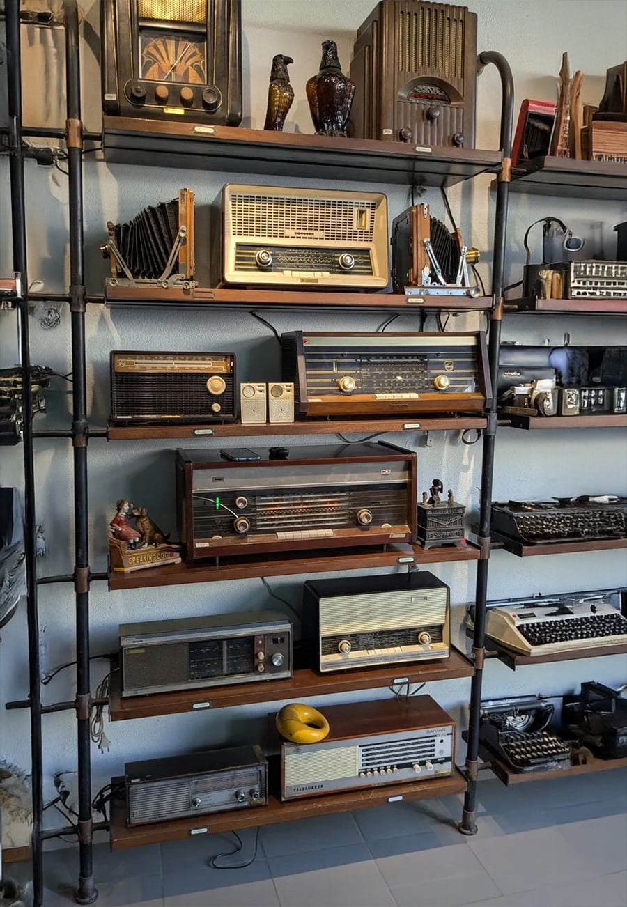 A shelving unit displays a collection of vintage radios, cameras, and typewriters, arranged neatly on wooden shelves with metallic frames, alongside small decorative items and retro electronics.