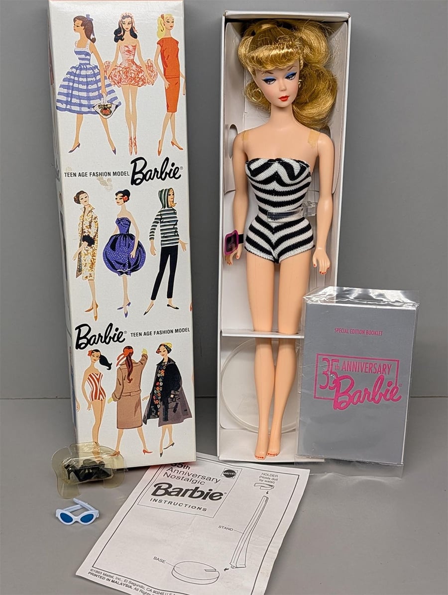 A vintage Barbie doll with blonde hair in a black and white striped swimsuit stands next to its box, which features illustrations of Barbie in various outfits. Accessories and instruction papers are laid out in front.