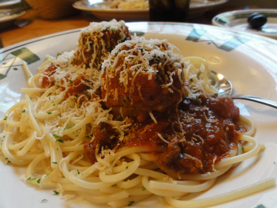 A plate of spaghetti topped with two large meatballs, marinara sauce, and grated cheese, served with a fork on the side.