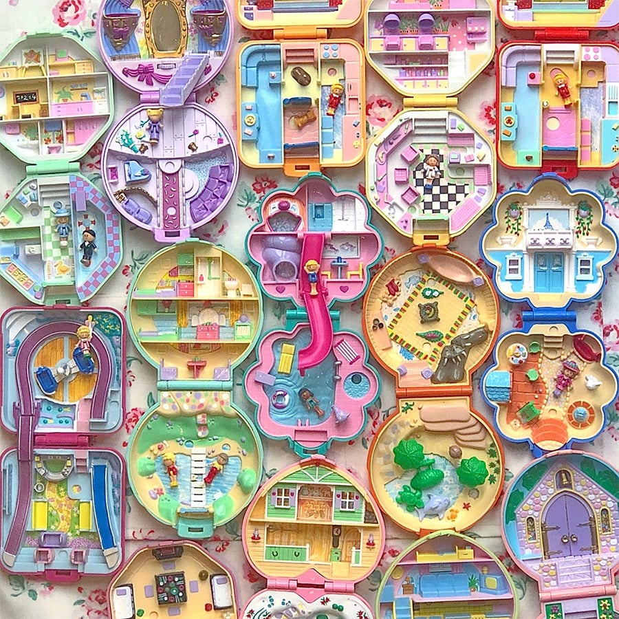 Colorful vintage Polly Pocket playsets, each open to reveal miniature dollhouse scenes with tiny furniture, characters, and detailed rooms, arranged in a neat grid on a floral background.