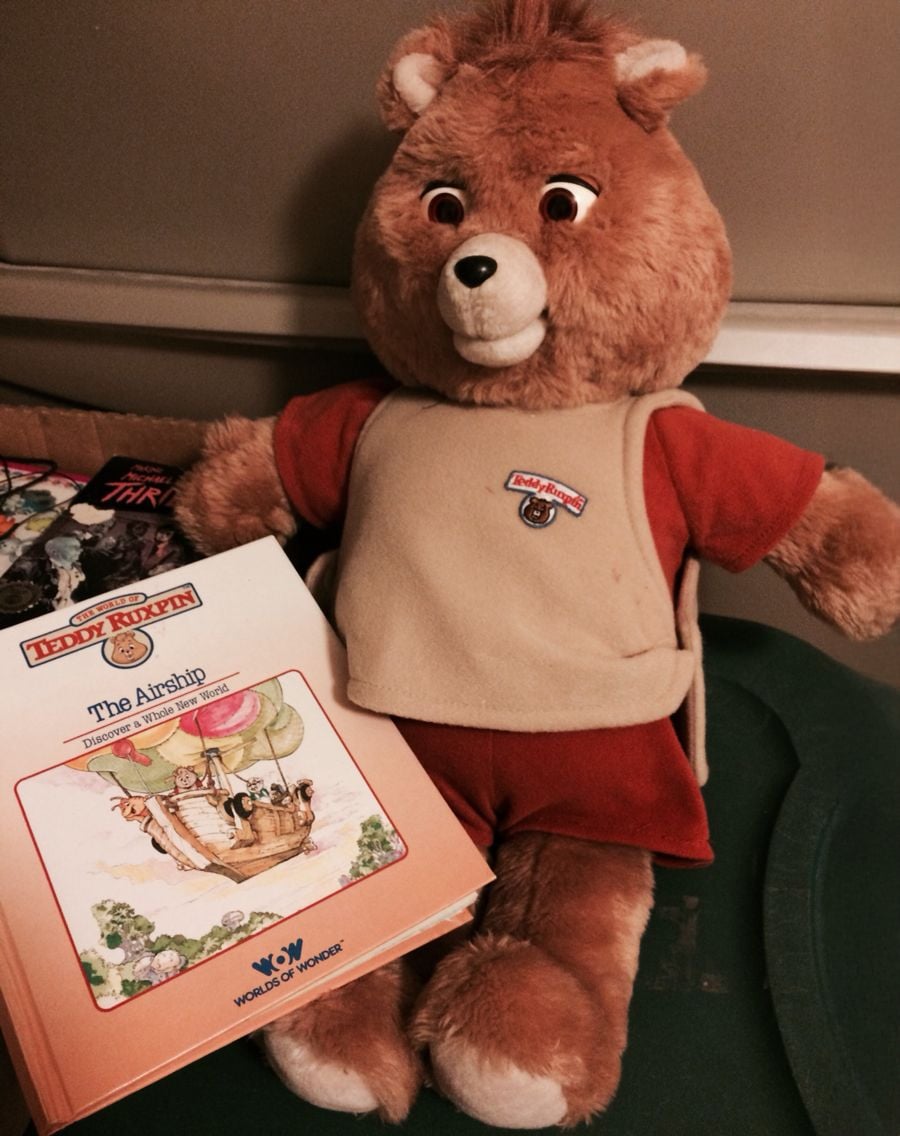 A Teddy Ruxpin bear plush toy wearing a tan vest and red shirt sits next to a children’s storybook titled "The Airship" from the Teddy Ruxpin series by Worlds of Wonder.