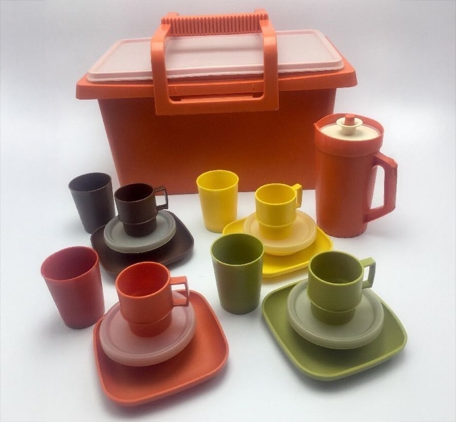 A vintage orange plastic picnic set with cups, mugs, plates, saucers, a jug with a lid, and a carrying case. The tableware comes in various colors, including yellow, brown, orange, and green.