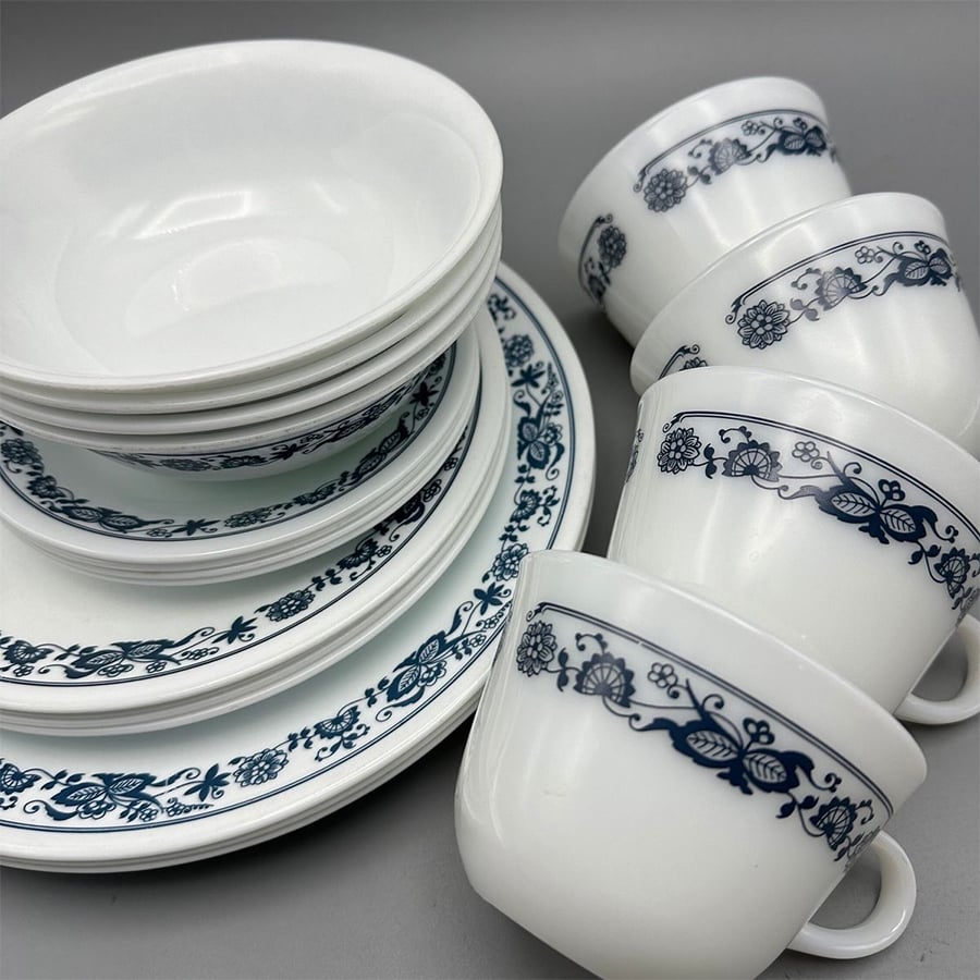 A stack of white bowls and plates with a blue floral pattern, next to four matching teacups, all arranged on a gray surface.