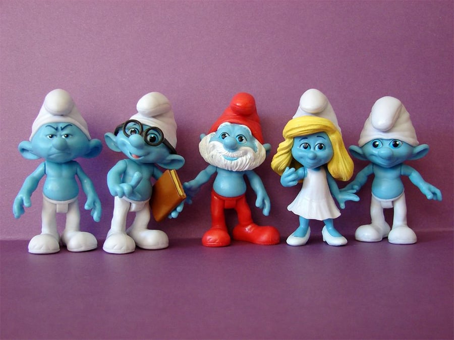 Five Smurf figurines stand in a row against a purple background, including Papa Smurf in red, Smurfette in a white dress, Brainy Smurf with glasses, and two other classic blue Smurf characters.