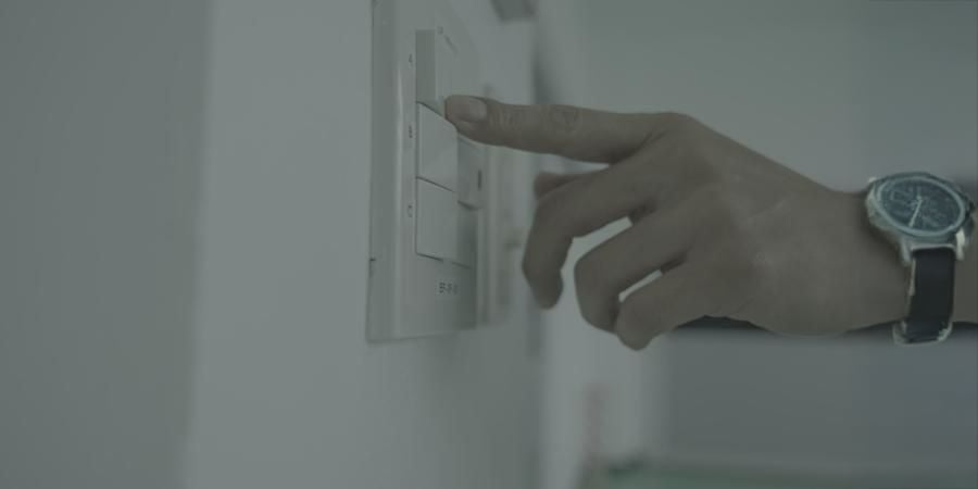A person wearing a wristwatch is pressing a button on a white wall switch panel with multiple labeled switches.