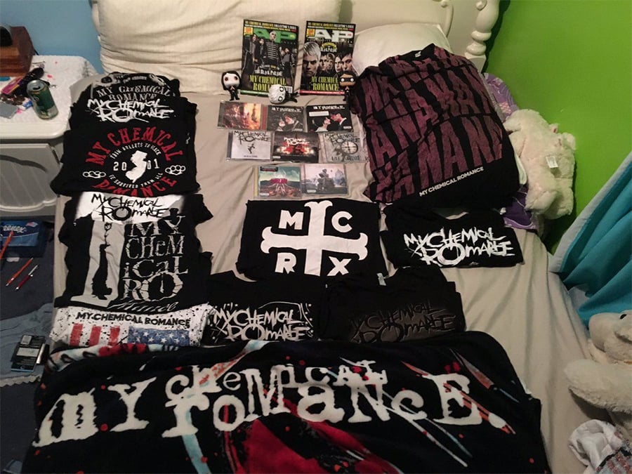 My Chemical Romance merchandise collection displayed on a bed, including band T-shirts, hoodies, CDs, magazines, Funko Pop figures, and other memorabilia, with a green wall and plush toys visible in the background.