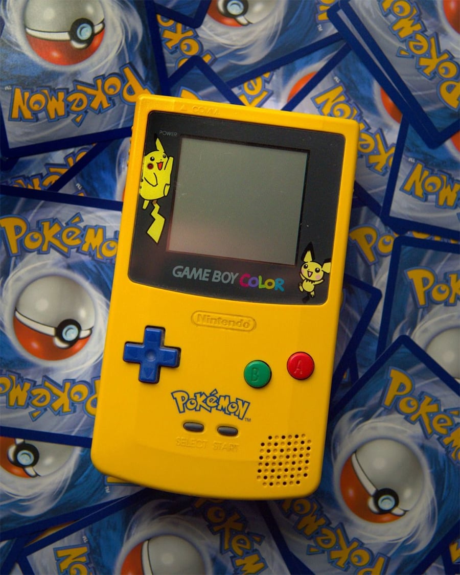 A yellow Pokémon-themed Game Boy Color featuring Pikachu and Pichu stickers lies on top of a scattered pile of Pokémon trading cards.