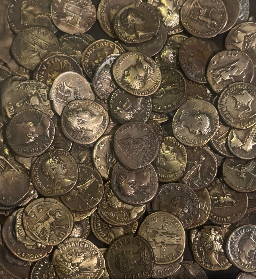 A pile of old, bronze Roman coins featuring various emperors’ profiles and symbols, some with Latin inscriptions and intricate designs, showing signs of age and wear.