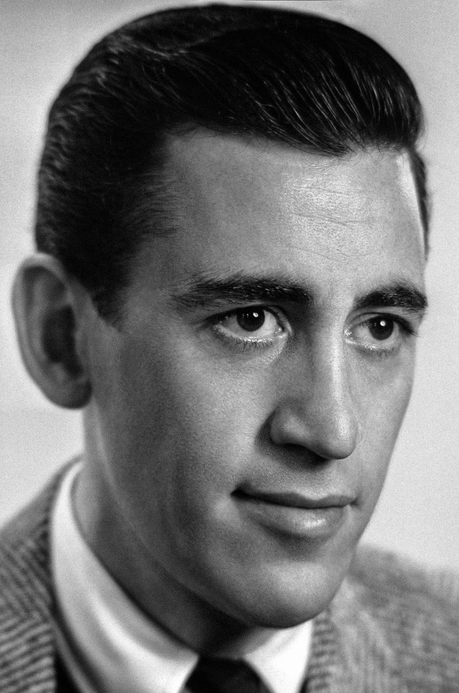 Black-and-white close-up portrait of a man with dark, neatly combed hair, wearing a suit jacket, white shirt, and tie, looking slightly to the side with a calm expression.