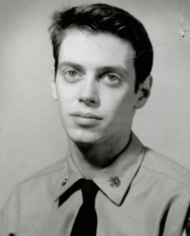 Black and white portrait of a young man with light eyes, short dark hair, and a neutral expression, wearing a uniform shirt and a tie.