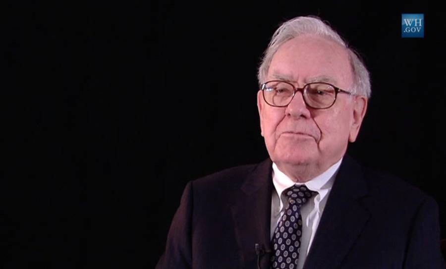 An older man with white hair and glasses, wearing a dark suit and polka dot tie, sits against a black background. A small blue logo with "WH.GOV" appears in the top right corner.
