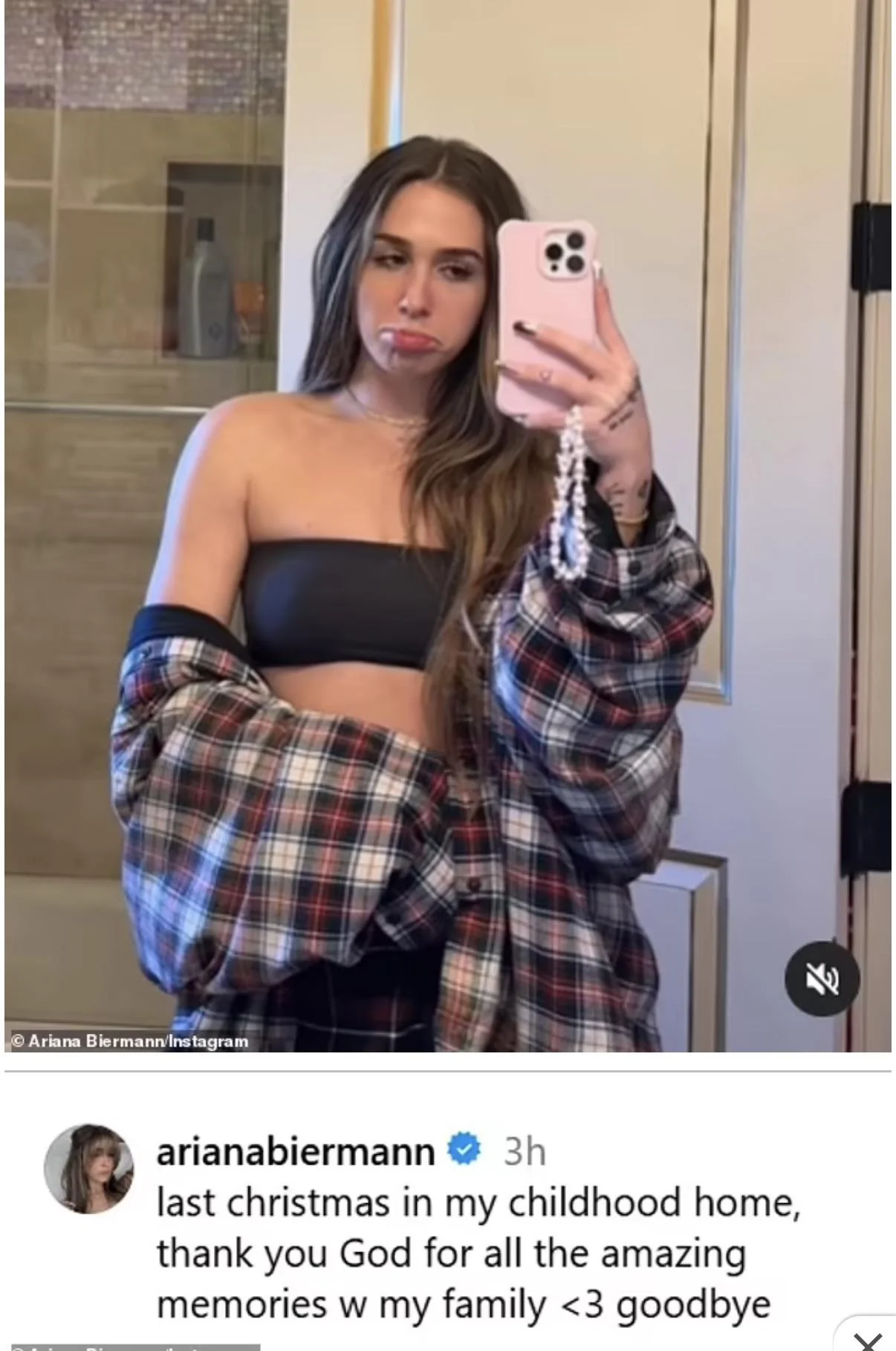 A young woman takes a mirror selfie in a bathroom, wearing a black tube top and an open plaid shirt. She has long hair and is pouting. An Instagram caption below mentions her last Christmas in her childhood home.