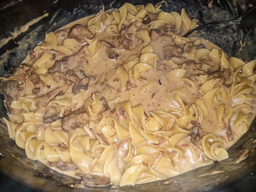 Creamy beef stroganoff with egg noodles in a thick sauce, showing chunks of beef and a rich, light brown sauce, all mixed together in a pot.