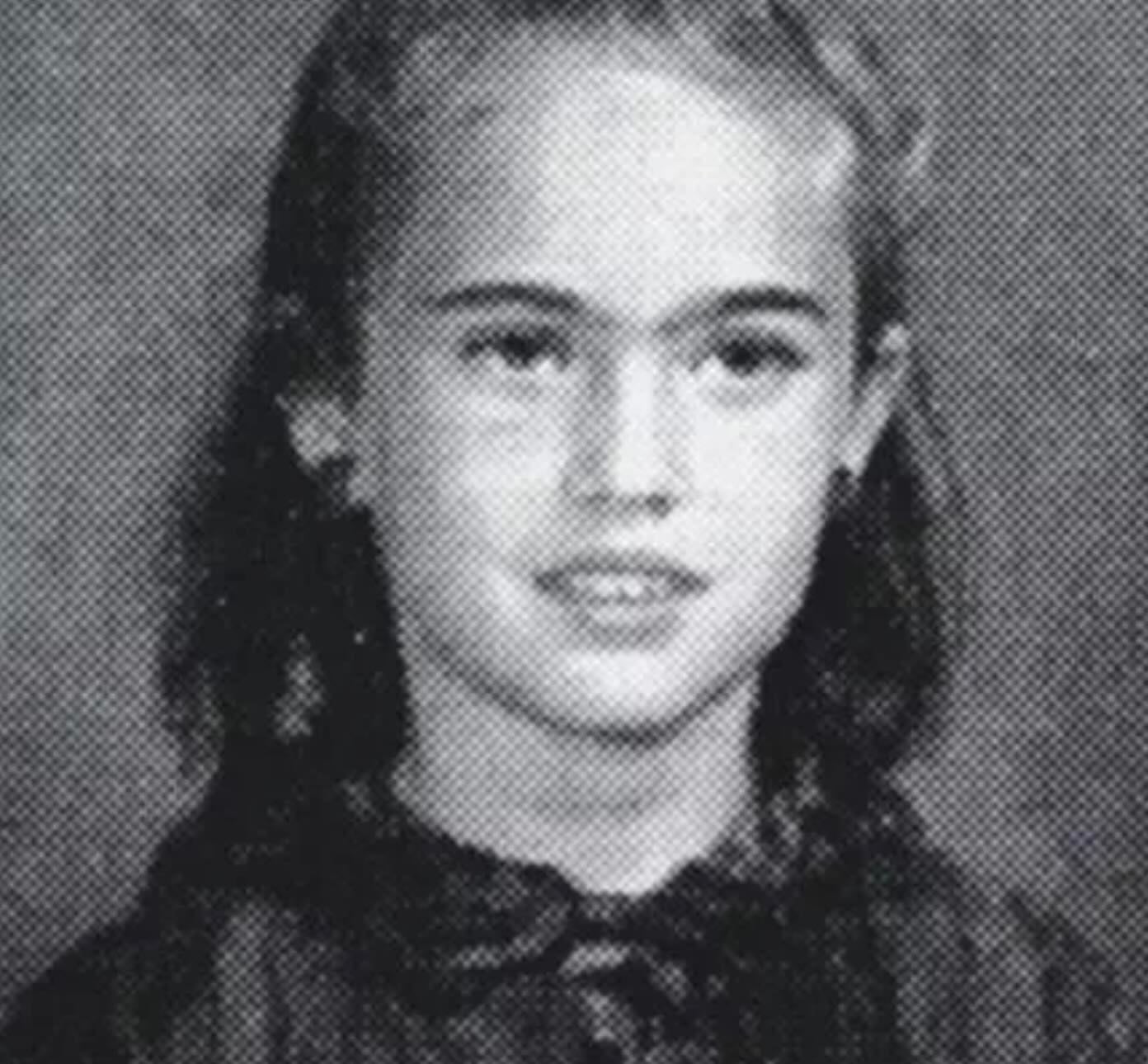 A black and white yearbook-style portrait of a young girl with long hair, wearing a dark top with a tied collar, looking at the camera with a slight smile.