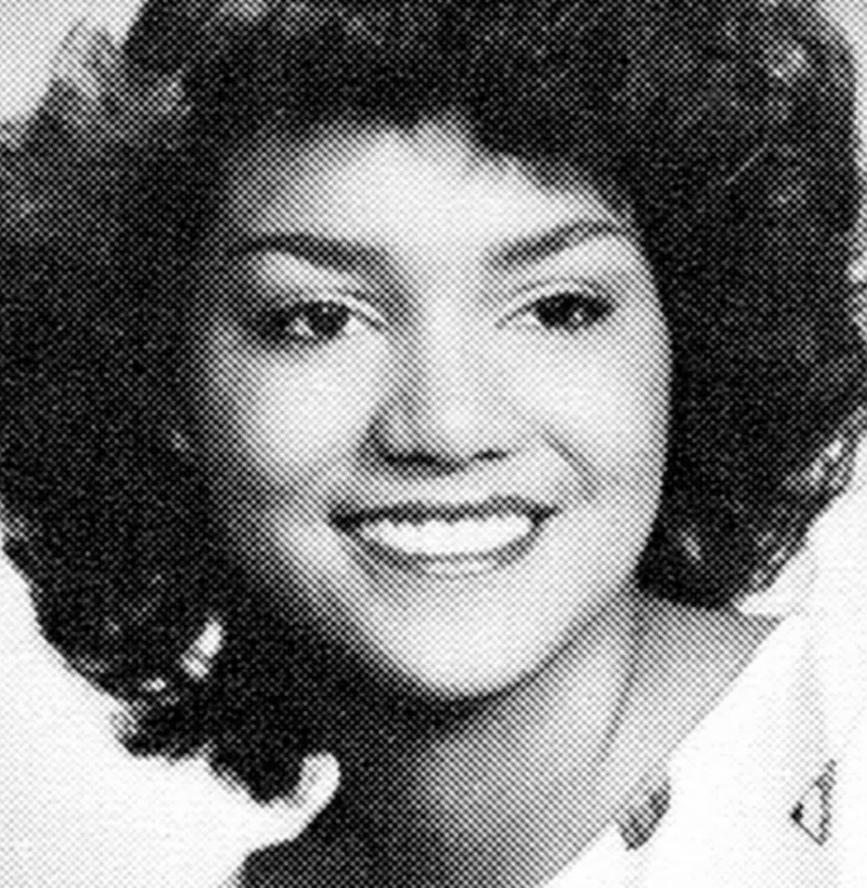 Black and white portrait of a young woman with curly hair, smiling, facing slightly to the side. She is wearing a light-colored top and appears to be in a school yearbook-style photo.