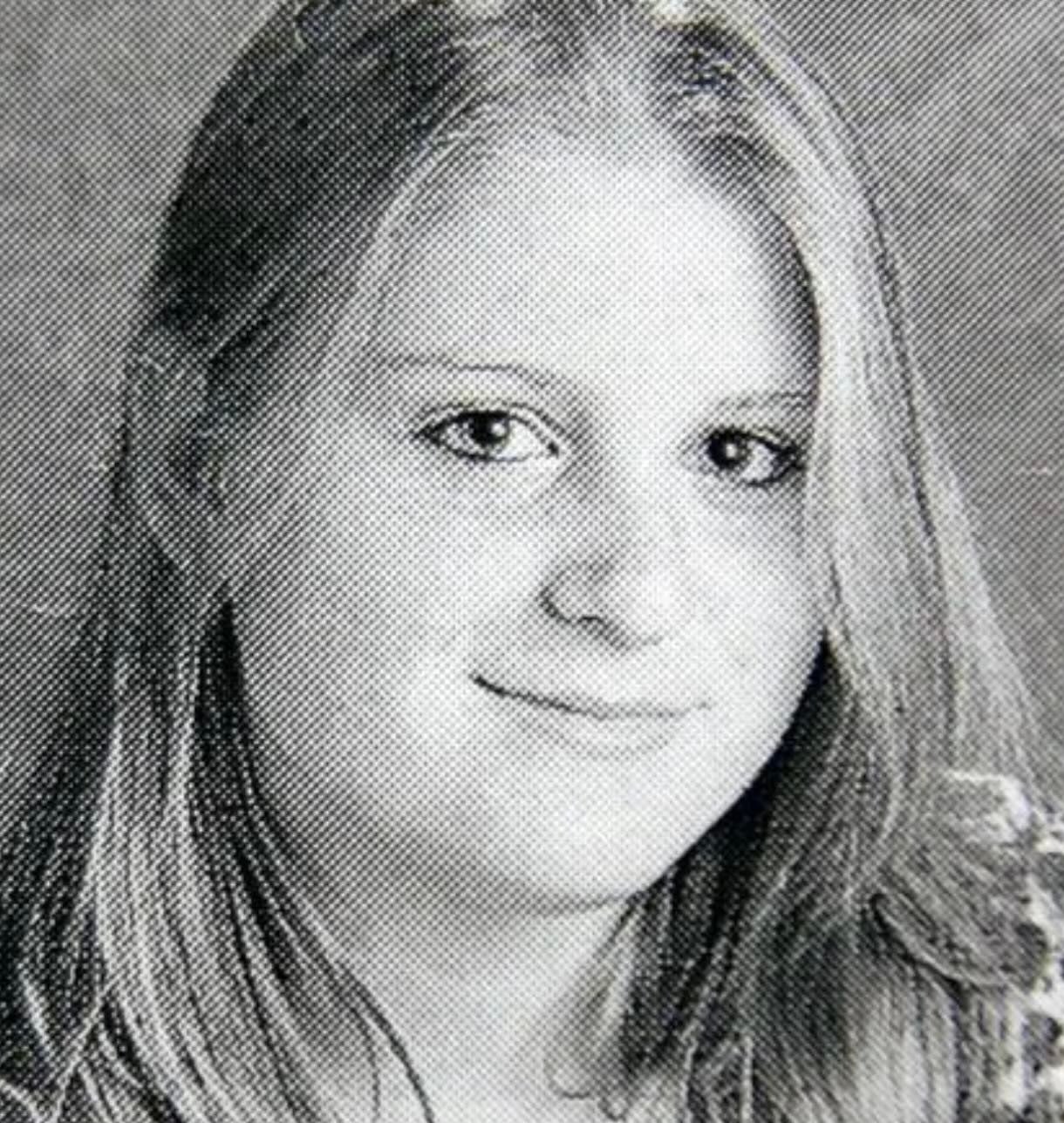 Black and white portrait of a young woman with long, straight hair, looking at the camera and softly smiling, against a plain background.
