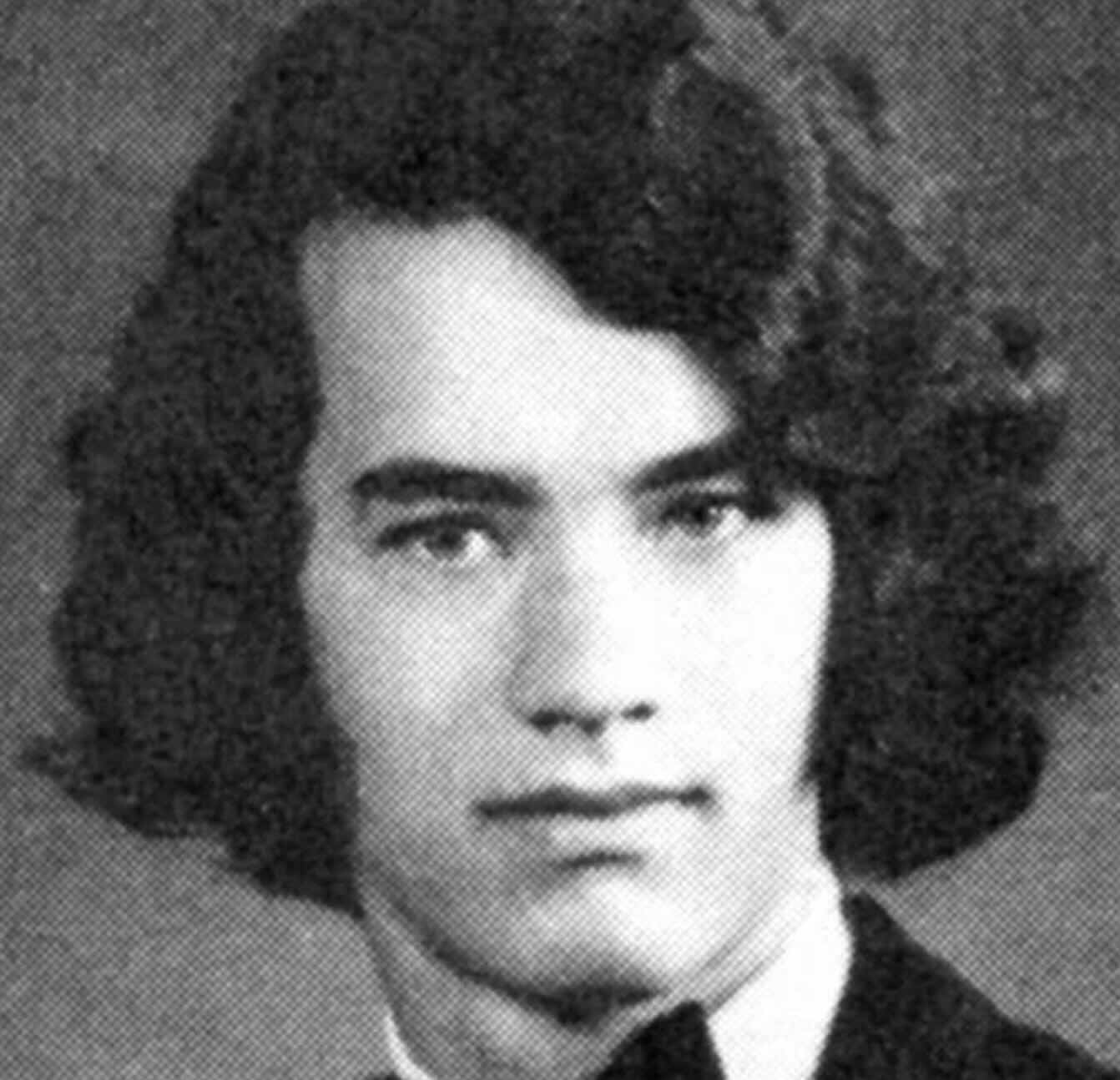 Black and white yearbook photo of a young man with medium-length, wavy dark hair, wearing a suit and bow tie, looking directly at the camera with a neutral expression.