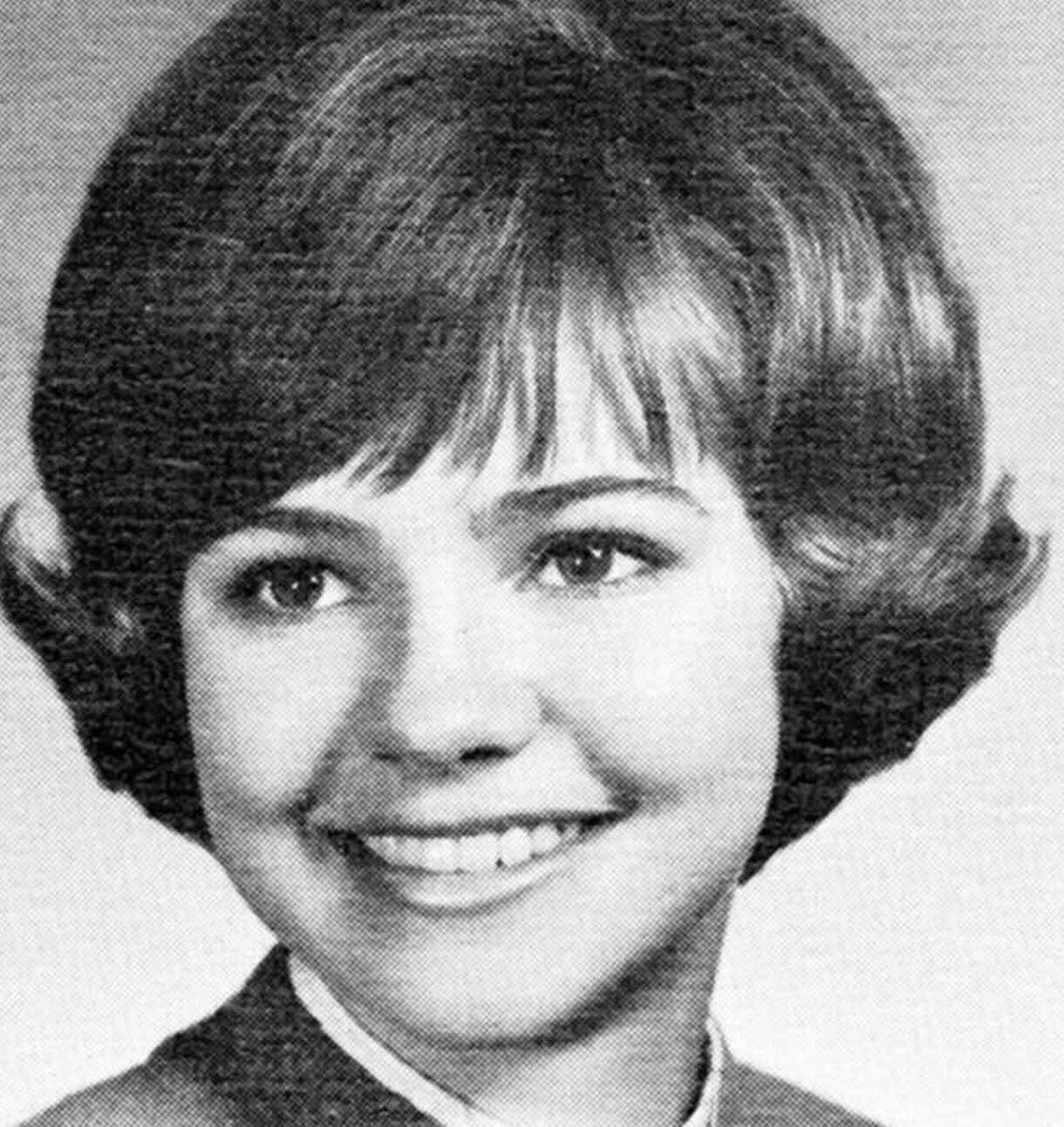Black-and-white portrait of a young woman with short, styled hair, smiling and looking slightly to the side. She is wearing a collared outfit, and the background is plain.