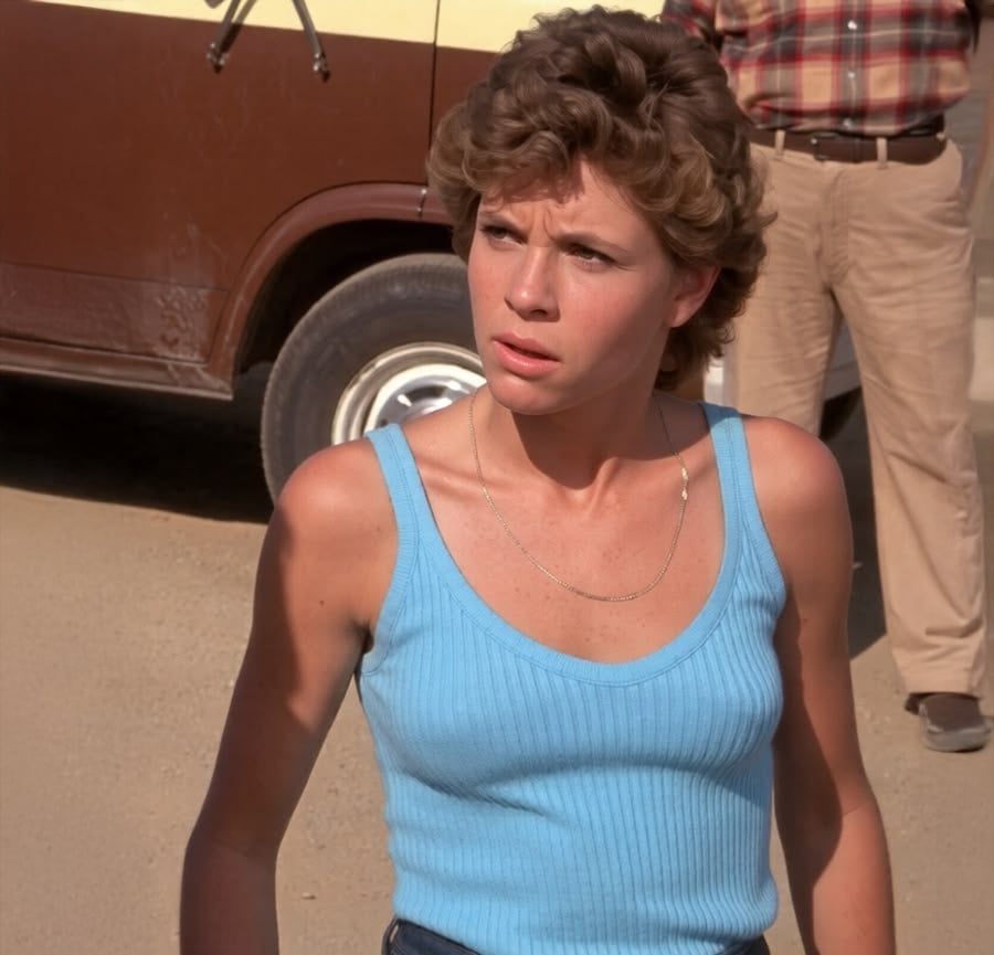 A young woman with short curly hair wearing a light blue tank top stands outdoors in front of a brown and cream van, looking slightly to the side with a concerned expression. A person in a plaid shirt stands behind her.