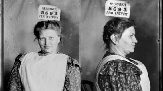 Black and white mugshot of a woman wearing a patterned dress and apron, shown front and side view, with a sign above her head reading &ldquo;Nebraska Penitentiary 5693.&rdquo;