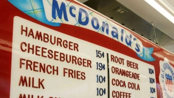 A vintage McDonald's menu displays items like hamburger for 15&cent;, cheeseburger for 19&cent;, and drinks such as root beer, orangeade, and milk, each priced at 10&cent;, with a red and white color scheme.