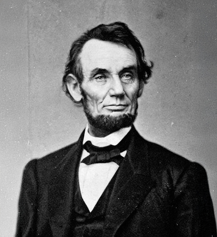 A black and white portrait of a man with a beard and mustache wearing a suit, bow tie, and white shirt, looking slightly to the side with a serious expression.