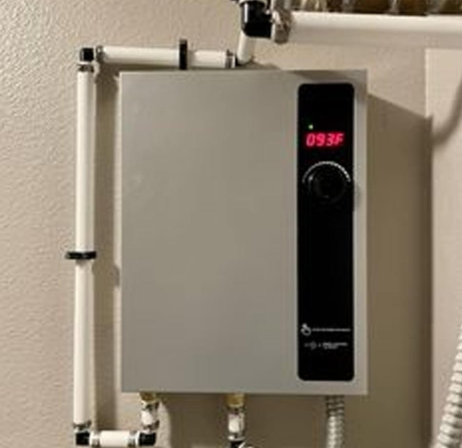 A wall-mounted tankless water heater with white pipes connected to it displays a digital temperature reading of 093°F on its front panel.