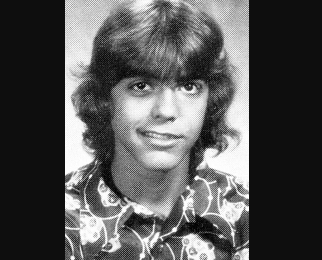 Black and white yearbook-style portrait of a young person with medium-length, wavy hair, wearing a collared shirt with a bold, patterned design. They are facing forward and smiling slightly.