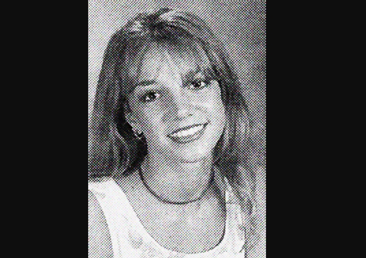 A black-and-white yearbook-style portrait of a young woman with long hair, wearing a sleeveless top and a choker necklace, smiling at the camera.