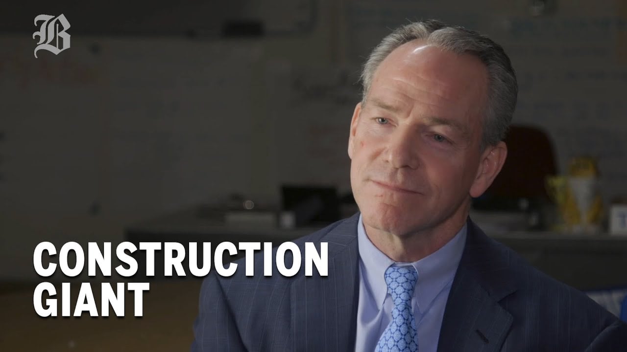 A man in a suit and blue tie sits and smiles slightly. The background is an office setting. White text in the lower left corner reads, "CONSTRUCTION GIANT." A stylized "B" logo appears in the top left.