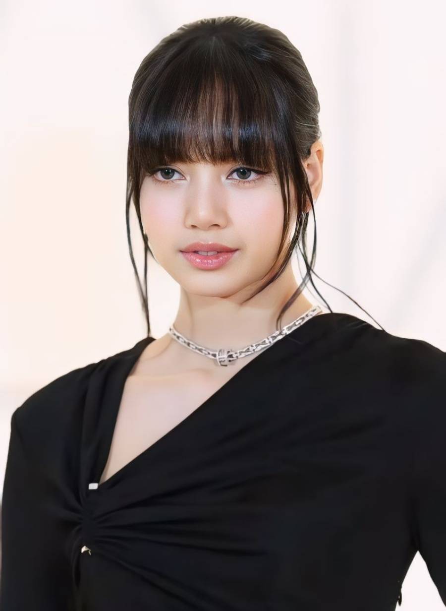 A young woman with straight black hair and bangs wears a black top with a gathered detail and a silver chain necklace. She is looking slightly to the side against a soft, light background.