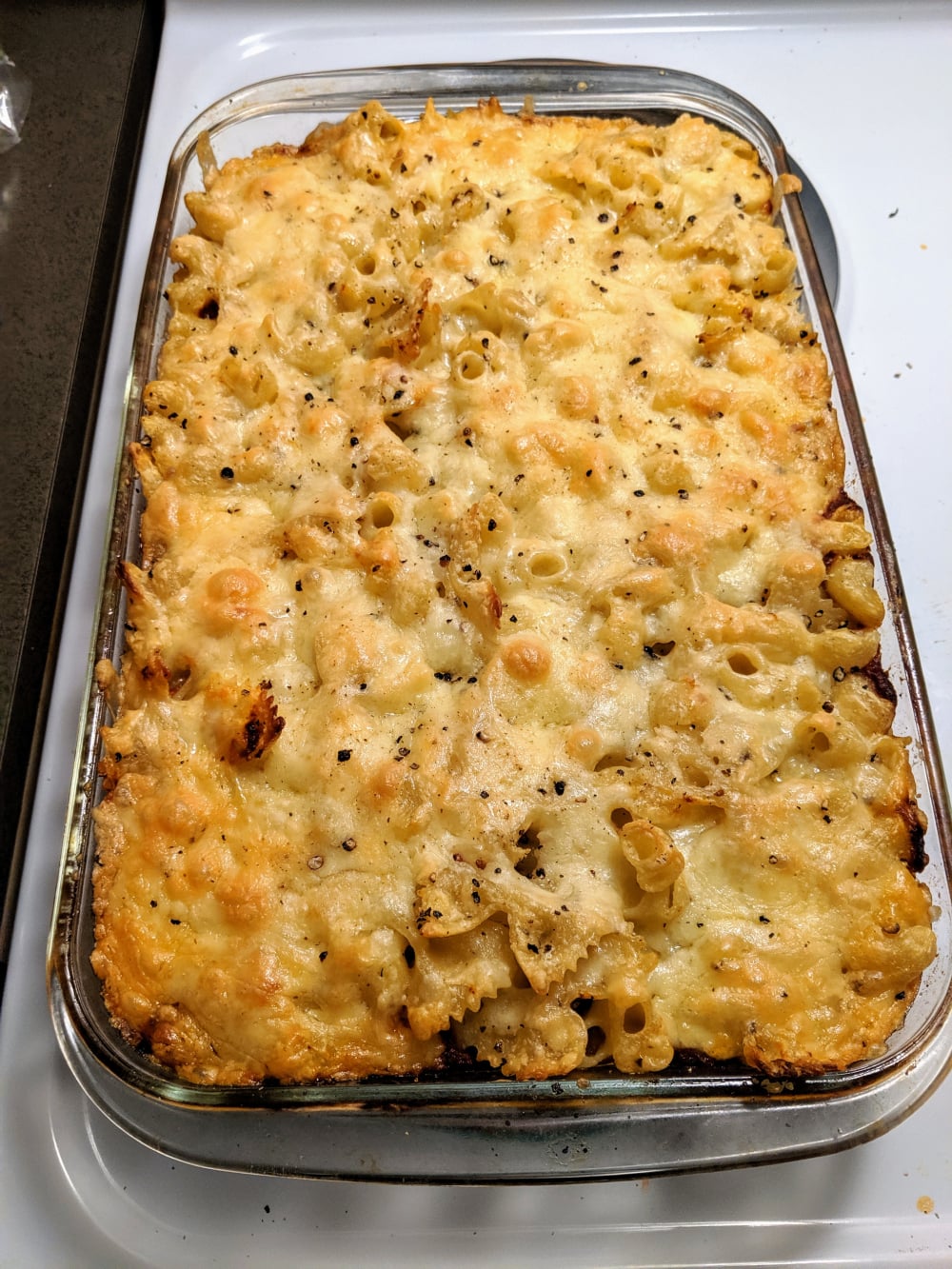 A glass baking dish filled with baked pasta topped with melted, golden-brown cheese sits on a stove, ready to be served.