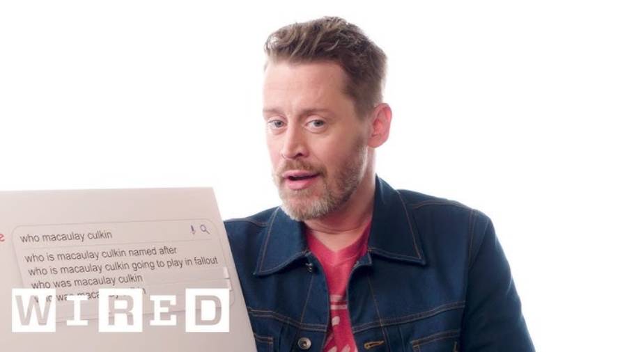 A man with light hair and a beard, wearing a denim jacket over a red shirt, holds a board showing Google search suggestions starting with "who macaulay culkin," with the Wired logo in the corner.