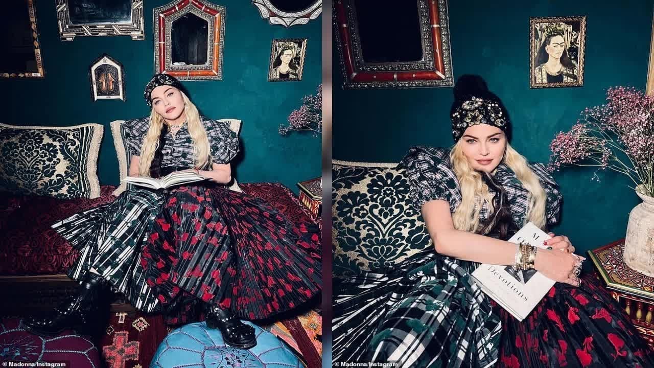 A woman with long blonde hair, wearing a black beanie, patterned dress, and boots, sits on a patterned sofa holding or reading a book. The wall behind her displays several ornate framed pictures and a vase of flowers.