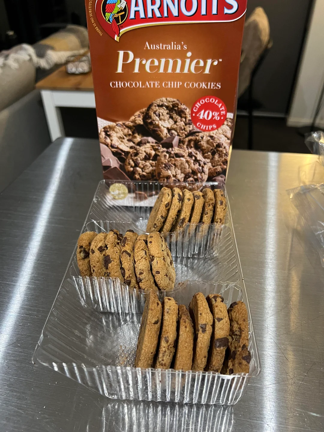 Open plastic tray of Arnott's Premier Chocolate Chip Cookies with several cookies stacked upright in rows, and the product box displayed behind the tray on a kitchen counter.