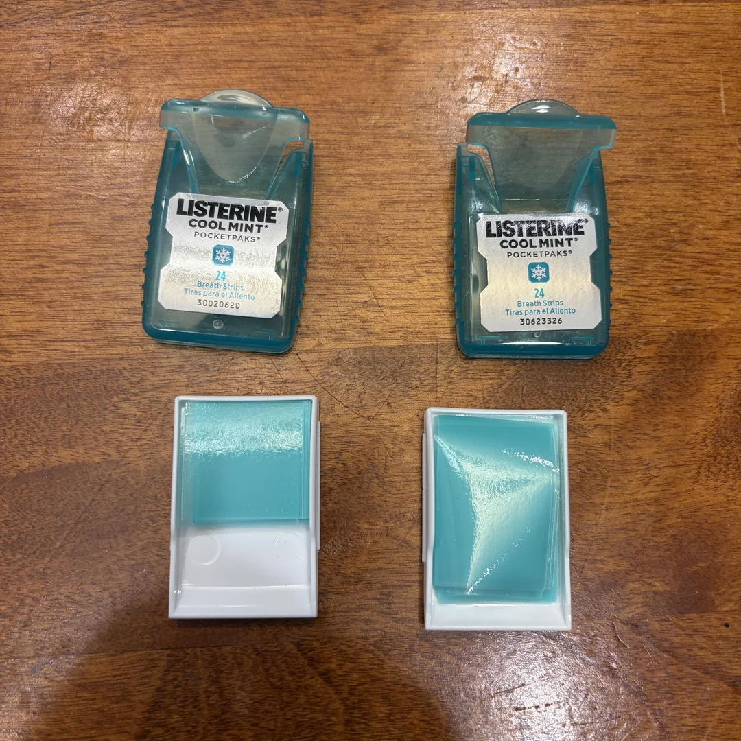 Two Listerine Cool Mint PocketPak containers are shown on a wooden surface. Below each open container are blue-green breath strips inside their white plastic holders.