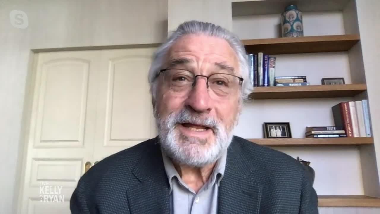 An older man with gray hair, glasses, and a beard speaks during a video call. He wears a dark blazer and sits in front of a bookshelf and double doors. The "LIVE Kelly and Ryan" logo appears in the bottom left corner.