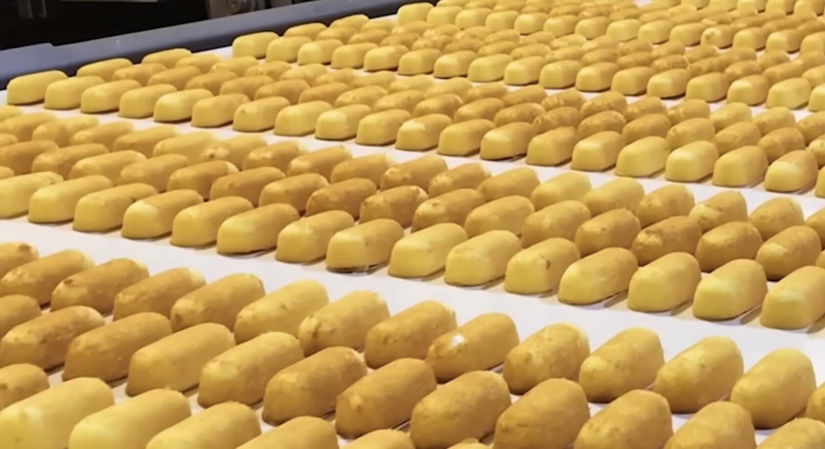 Rows of golden yellow snack cakes are lined up neatly on a conveyor belt in a factory setting, ready for packaging.
