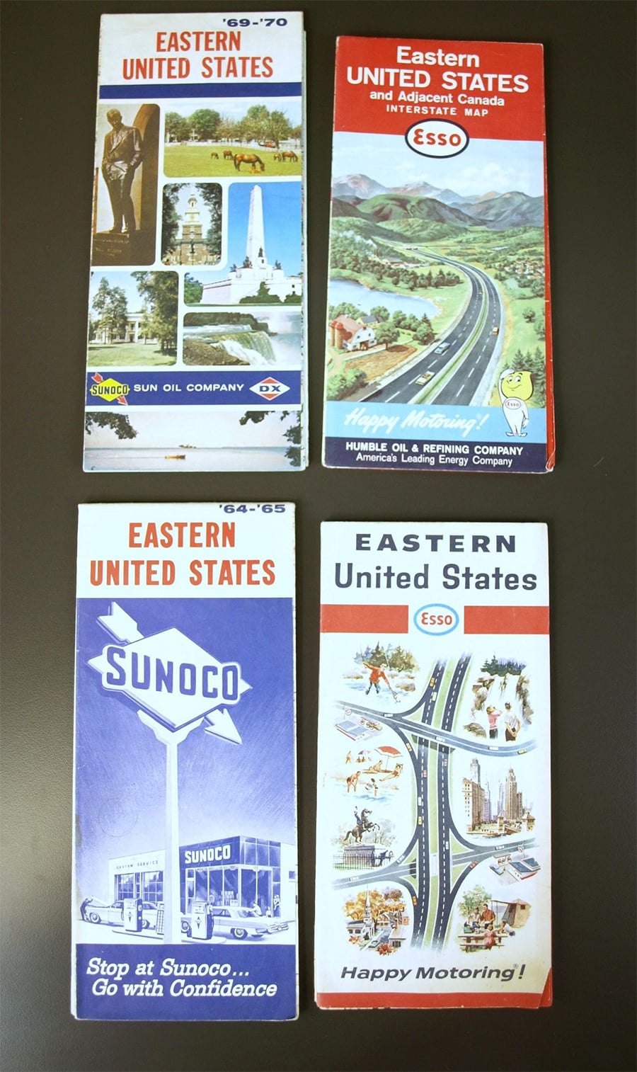 Four vintage road maps of the Eastern United States are arranged on a flat surface, each featuring colorful illustrations and logos from Sun Oil Company and Esso on their covers.