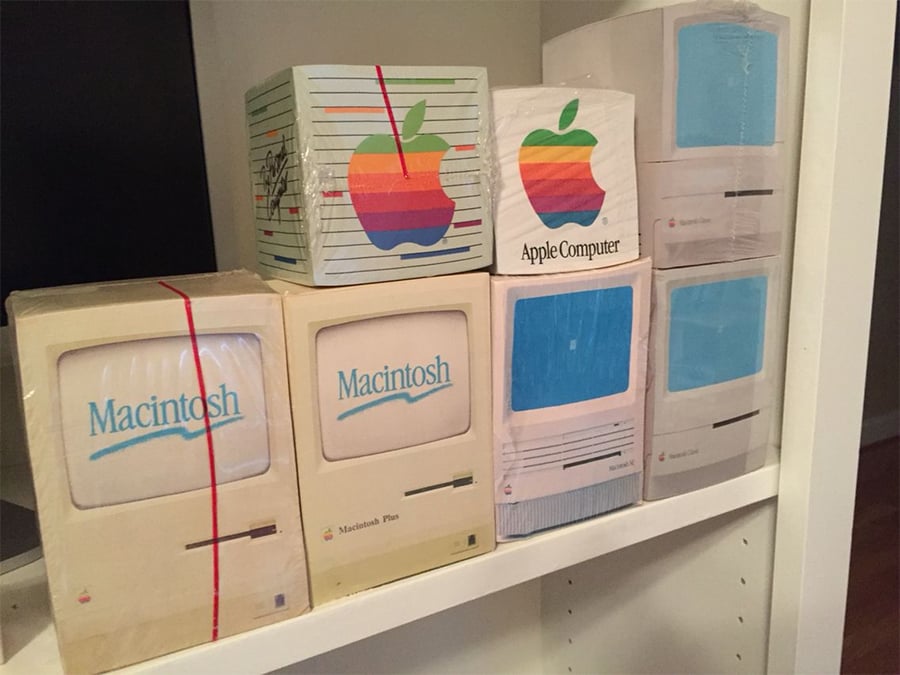 Several vintage Macintosh computer boxes are displayed on white shelves, featuring colorful Apple logos and old-style packaging designs, including the Macintosh Plus and other classic Apple models.