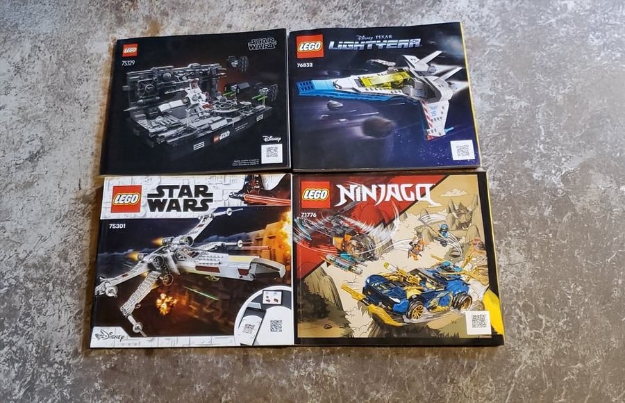 Four LEGO instruction booklets are laid out on a textured surface. Sets include Star Wars, Lightyear, and Ninjago themes, with spaceship and vehicle artwork on each booklet cover.