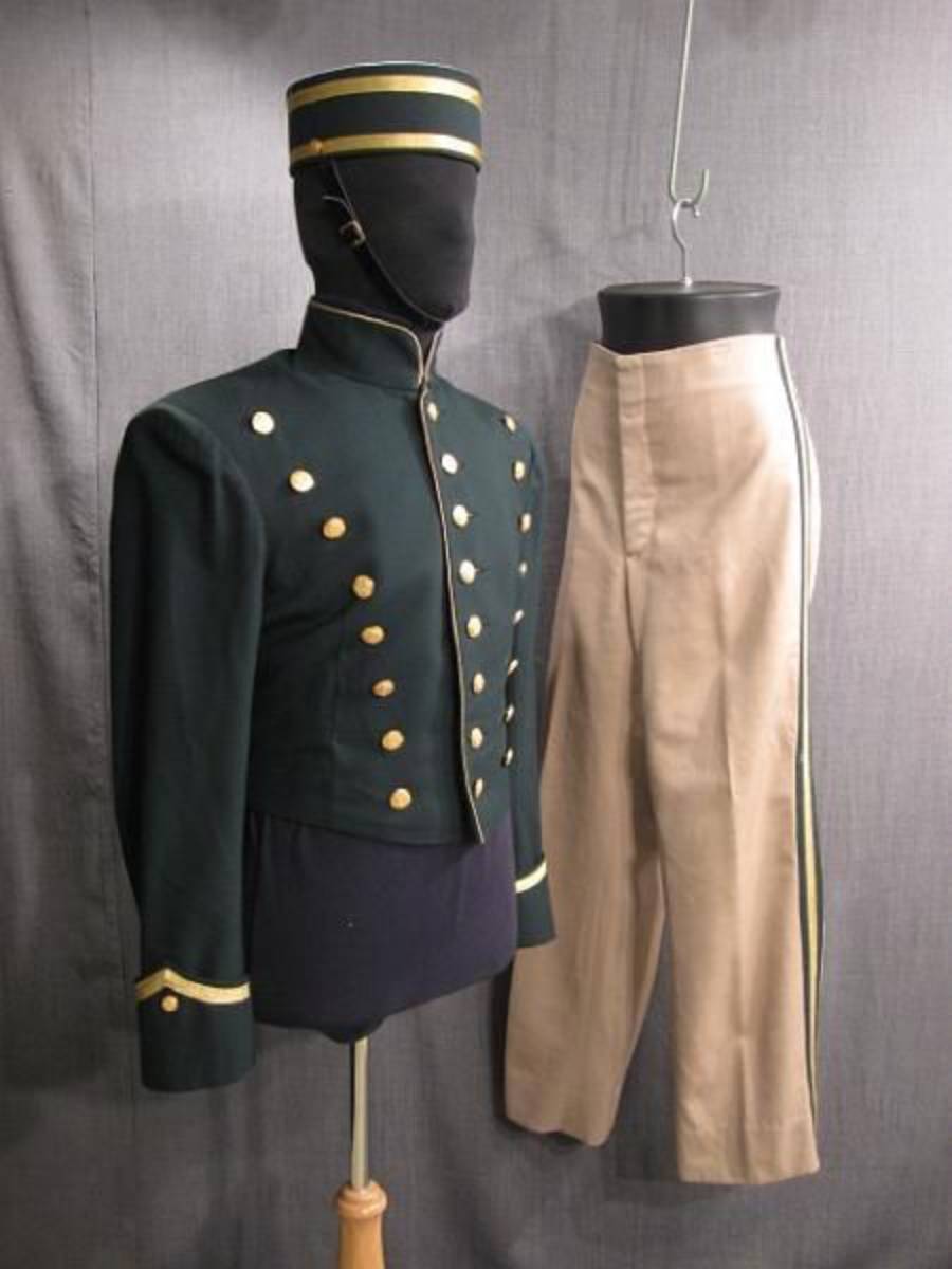 A mannequin displays a dark green, double-breasted uniform jacket with gold buttons and trim, alongside tan trousers with a matching green and gold stripe, and a matching green and gold cap.