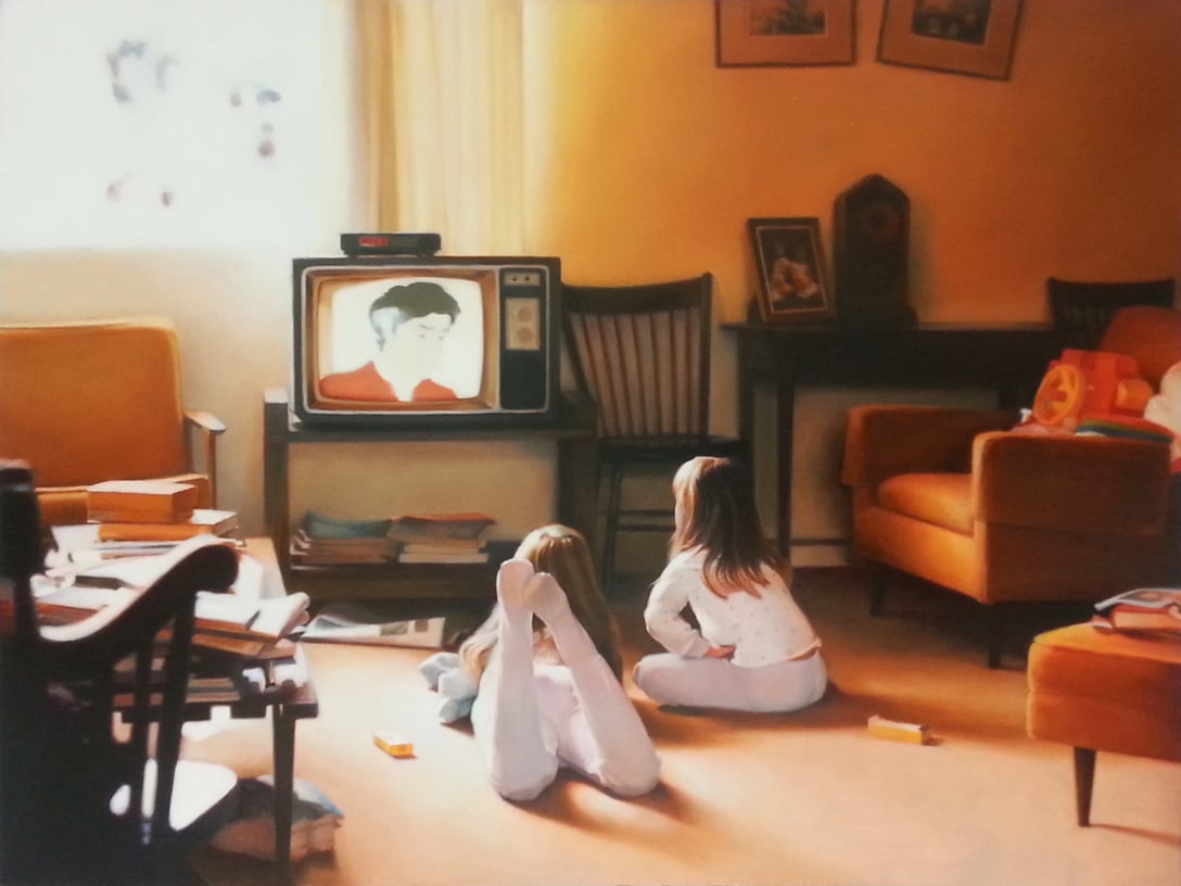 Two young girls in pajamas lie on the floor of a cozy living room, watching a vintage television. The room has warm lighting, orange chairs, a table with books, and framed photos on the walls.