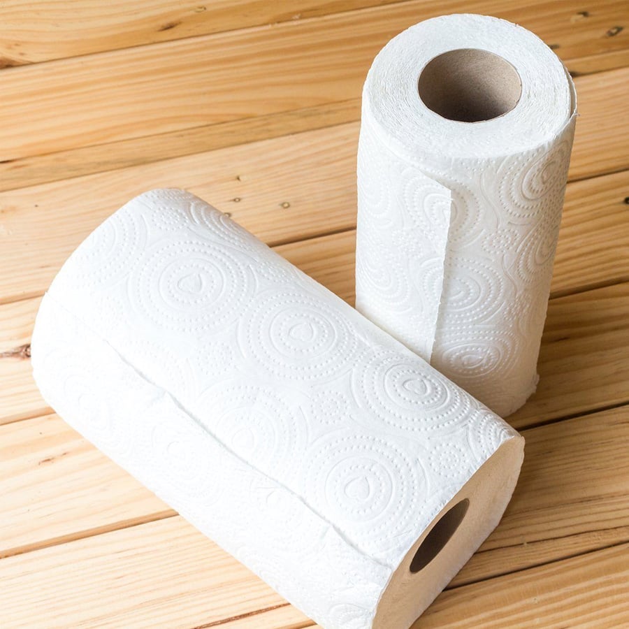 Two rolls of white paper towels, one standing upright and the other lying down, on a light wooden surface.