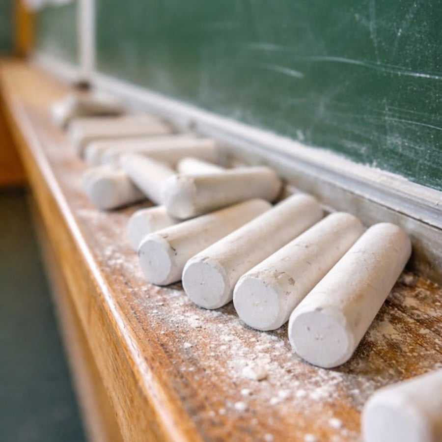 Several pieces of white chalk rest on a wooden ledge beneath a green chalkboard, with chalk dust scattered around.