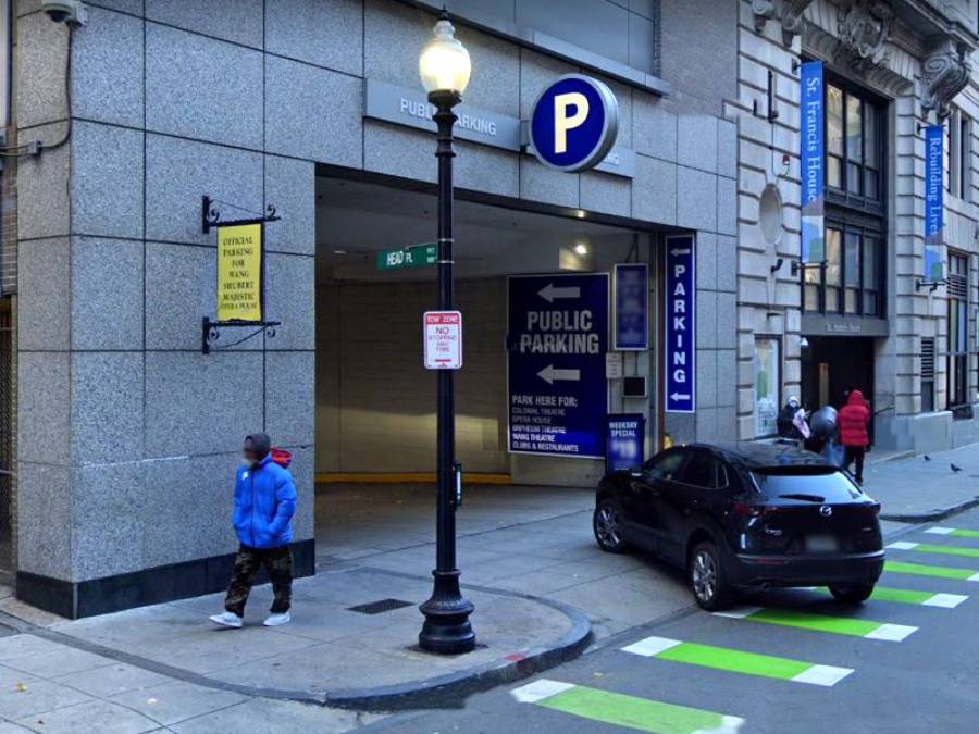 A public parking garage entrance with a blue "P" sign, a black car parked at the curb, pedestrians nearby, and green-striped bike lanes painted on the street.