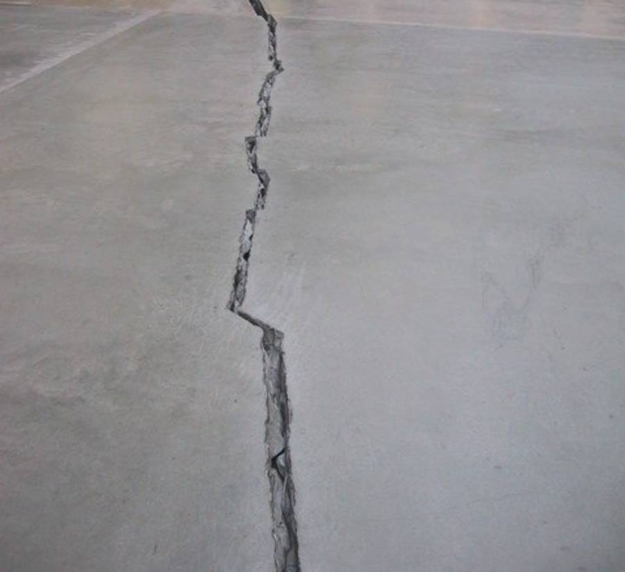 A large, jagged crack runs through the middle of a smooth concrete floor, splitting the surface and indicating structural damage.