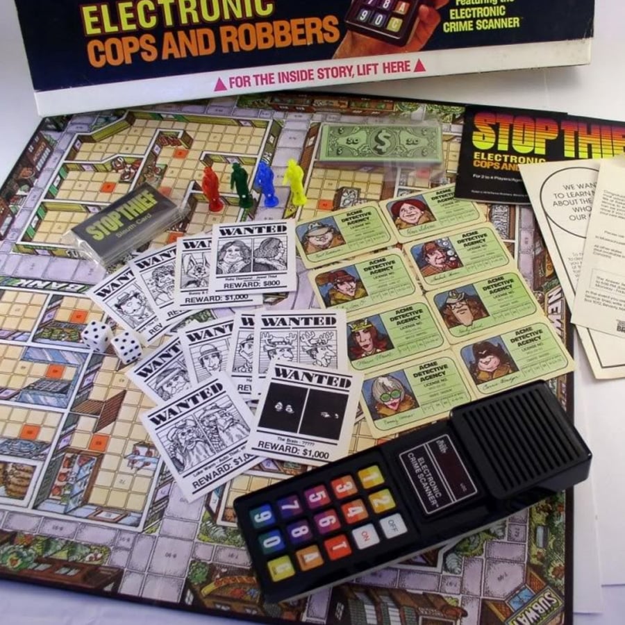 An electronic board game called Cops and Robbers is displayed with cards, money, player tokens, dice, “WANTED” posters, and an electronic crime scanner device on the game board.