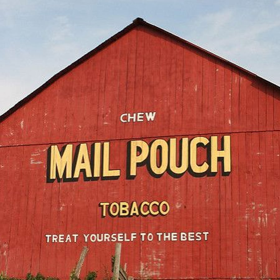 A red barn with the words "Chew Mail Pouch Tobacco" and "Treat yourself to the best" painted in large yellow and white letters on the side. Blue sky is visible above the roof.